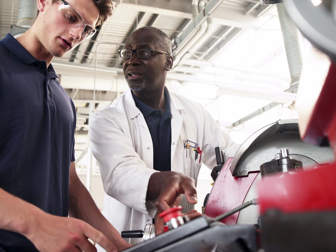 An experienced engineer showing an apprentice how to operate a machine on a factory floor.